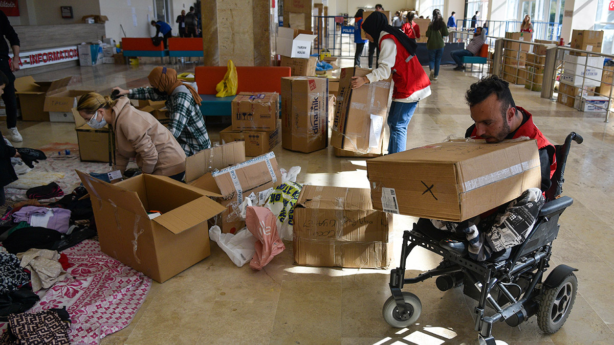 Antalya'ya gelen depremzedelerin kayıt yaptırıp, ihtiyaçları karşılandıktan sonra konaklayacağı tesise yönlendirildiği spor salonundaki çalışmalara gönüllü katılan bedensel engelli şampiyon yüzücü Sefa Yurtkölesi (28), akülü tekerlekli sandalyesiyle yardım kolisi taşıyarak taşıyamadıklarını da aracıyla iterek çalışmalara destek veriyor.