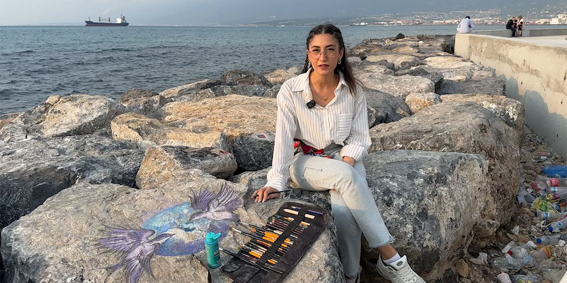 Kahramanmaraş merkezli 6 Şubat 2023'teki depremlerde Hatay’ın İskenderun ilçesinde yıkılan binanın enkazından kurtarılan ressam Edanur Sarar (25), afetin etkilerini unutmak ve unutturmak için sahildeki kayalara renkli figürler çiziyor.
