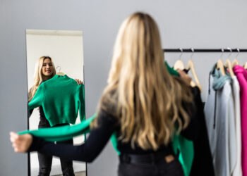 Young woman looking into mirror near wardrobe at home