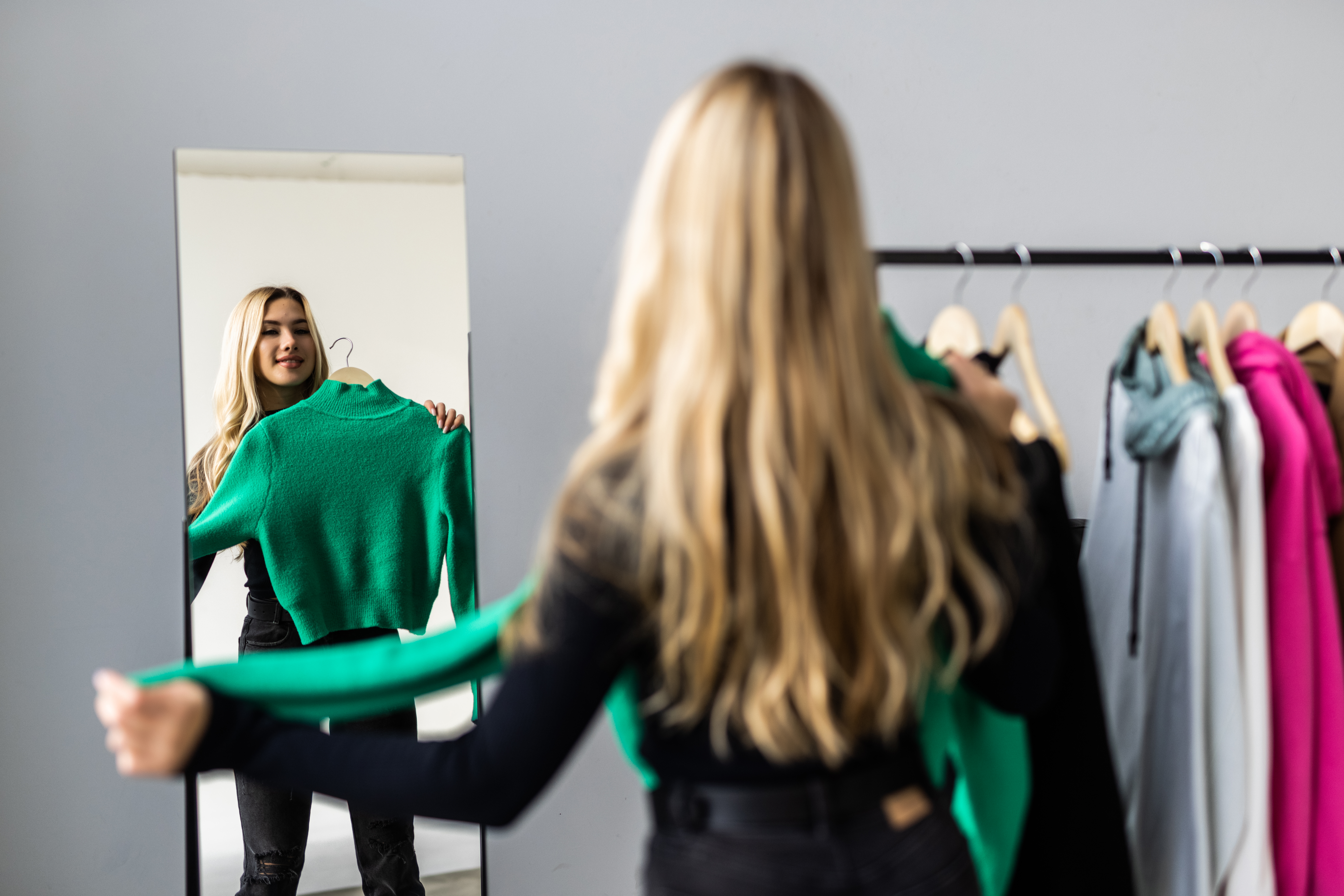 Young woman looking into mirror near wardrobe at home