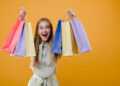 beautiful happy smiling blonde girl with colorful shopping bags isolated over yellow