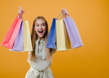 beautiful happy smiling blonde girl with colorful shopping bags isolated over yellow