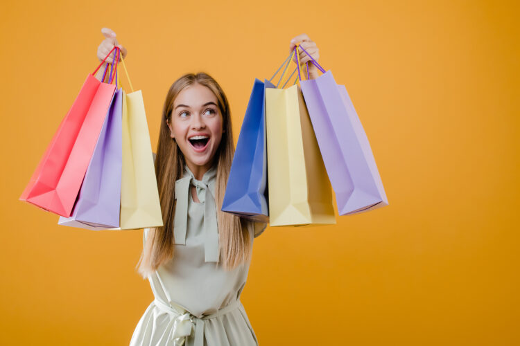 beautiful happy smiling blonde girl with colorful shopping bags isolated over yellow