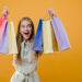beautiful happy smiling blonde girl with colorful shopping bags isolated over yellow