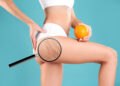 Cellulite problem. Slim woman in underwear holding orange on light blue background, closeup. Zoomed skin with dimples, view through magnifying glass
