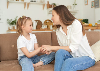 The little girl complains to her mother and cries. A young woman calms her daughter on the couch at home.