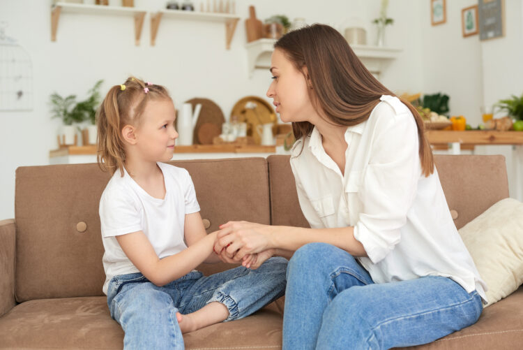 The little girl complains to her mother and cries. A young woman calms her daughter on the couch at home.