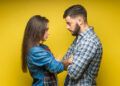 Photo of angry man and woman in denim clothes being in fight and standing with arms folded isolated over yellow background.