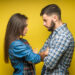 Photo of angry man and woman in denim clothes being in fight and standing with arms folded isolated over yellow background.
