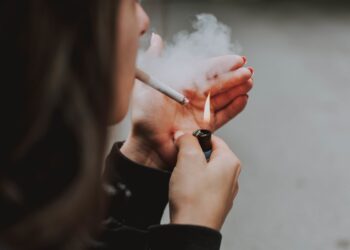 A selective closeup shot of a female lighting up a cigarette with a lighter