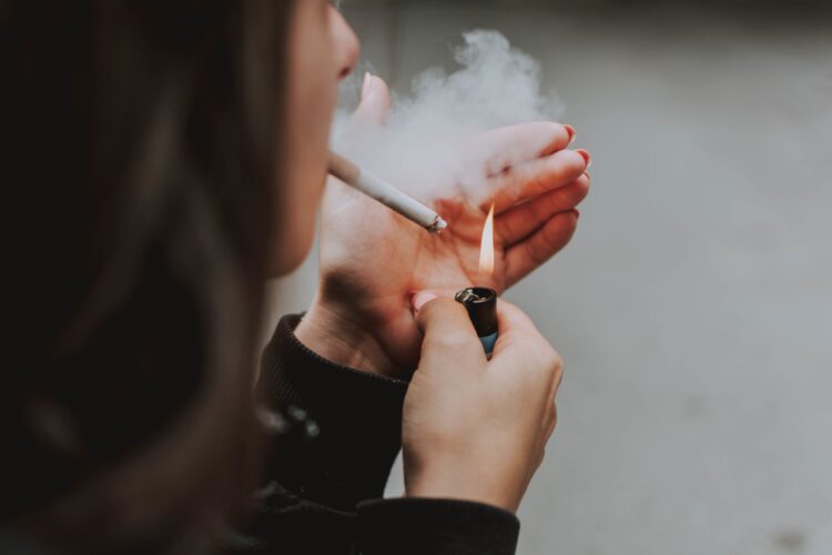 A selective closeup shot of a female lighting up a cigarette with a lighter