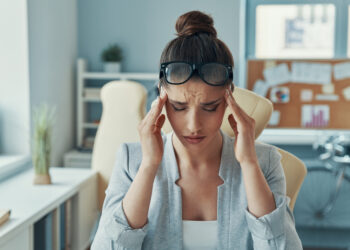 Stressed young woman in smart casual wear keeping head in hands while sitting in the office