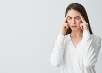 Young beautiful brunette businesswoman holding fingers on temples frowning from pain over white background. Headache. Copy space.
