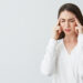 Young beautiful brunette businesswoman holding fingers on temples frowning from pain over white background. Headache. Copy space.