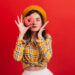 Young girl in great mood covers her eyes with strawberry donut. Woman with red lips in beret posing with closed eyes on isolated background
