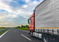 A red cargo truck drives on a highway beside a gray trailer, with open lanes and countryside visible. Useful for freight transport articles, logistics marketing, trucking content, and road infrastructure materials. SSUCv3H4sIAAAAAAAAA41Py46DMAz8F5+DFGihaX6l6sEhLrUKpEpMqxXKv69Cqfa6txnb8/AK7MFCc75hdzK66siYqq5vdWWocVXrHHp3ojPqBhR4FAJbH45N15m2M8f2YLTWWoHDxD3YFXgclyQRhcMMViuINHuKGyTPEiLjCFZnBUlQlkQJ7JoV9Cg0hMgb//pd1jIHC6AgLa6ArP45uyrAgeb+p/jnUmQk3OIuVwWPt1Cc9uwg91KxwGfknudh77QkCdMHz0GKdkuQ0D/Y7+LPG3dOEmLJguU5BvTk9/XiJhb50kgvpvffdc75F/TyQcyEAQAA
